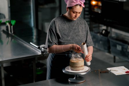 Foto de Panadero femenino en una cocina profesional envuelve un pastel casi terminado en película de aferramiento - Imagen libre de derechos