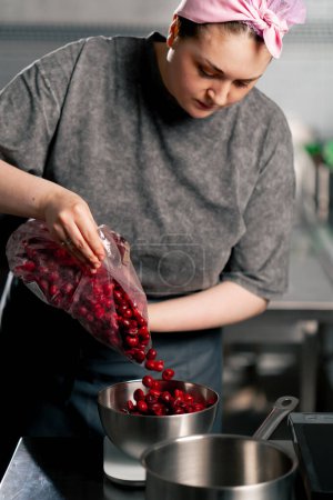 Photo for Female baker in a professional kitchen pours frozen cherries into a bowl on a scale - Royalty Free Image
