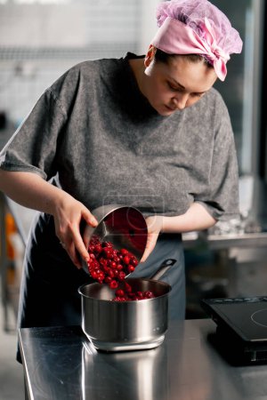 Téléchargez les photos : Femme boulangère dans une cuisine professionnelle verse des cerises congelées dans un bol sur une échelle - en image libre de droit