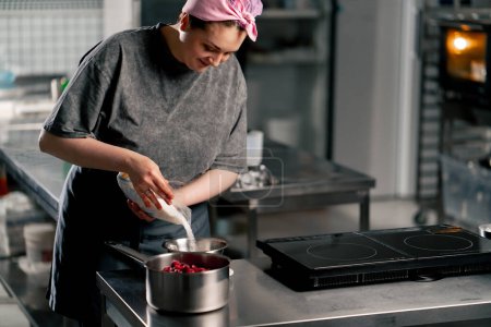 Téléchargez les photos : Femelle boulanger dans la cuisine professionnelle verse le sucre dans un bol pour la cuisson - en image libre de droit