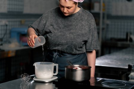 Foto de En la cocina profesional vierte agua en un recipiente de medición para la masa - Imagen libre de derechos