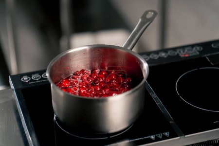 Téléchargez les photos : Gros plan dans la cuisine professionnelle des cerises bouillantes dans une casserole sur la cuisinière - en image libre de droit