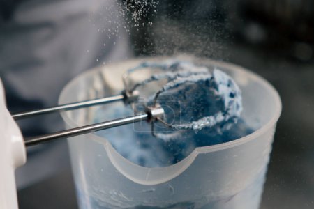 Photo for Close-up in a professional kitchen a baker pours powdered sugar onto blue cream - Royalty Free Image