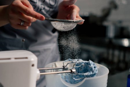 Foto de Primer plano en una cocina profesional un panadero vierte azúcar en polvo sobre la crema azul - Imagen libre de derechos