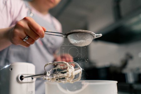 Foto de Primer plano de una panadera en una cocina profesional espolvorea con azúcar en polvo a través de un tamiz - Imagen libre de derechos