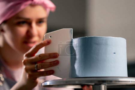 Foto de Primer plano panadero femenino en una cocina profesional distribuye crema azul en un pastel de esponja con una espátula - Imagen libre de derechos