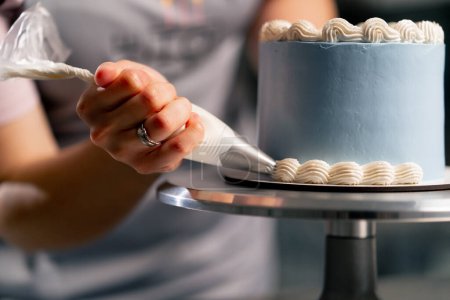 Téléchargez les photos : Gros plan d'une boulangère dans une cuisine professionnelle décorant un gâteau bleu avec de la crème - en image libre de droit