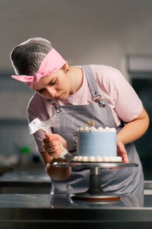 Téléchargez les photos : D'une boulangère dans une cuisine professionnelle décorant un gâteau bleu avec de la crème - en image libre de droit