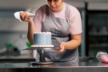 Foto de De una pastelera en una cocina profesional decorando un pastel azul con crema - Imagen libre de derechos