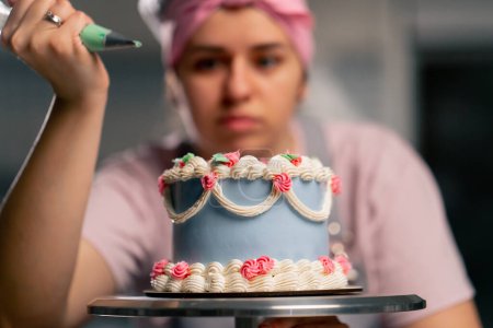 Foto de Primer plano de una panadera en una cocina profesional decorando un pastel azul con crema - Imagen libre de derechos