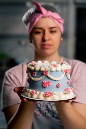 Foto de Primer plano en una cocina profesional un panadero femenino se para con un pastel terminado en sus manos - Imagen libre de derechos