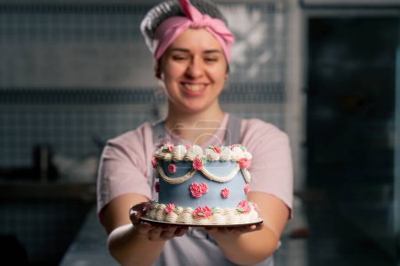 Foto de Primer plano en una cocina profesional un panadero femenino se para con un pastel terminado en sus manos ella sonriendo - Imagen libre de derechos
