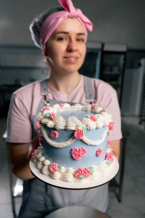 Foto de Primer plano en una cocina profesional un panadero femenino se para con un pastel terminado en sus manos ella sonriendo - Imagen libre de derechos