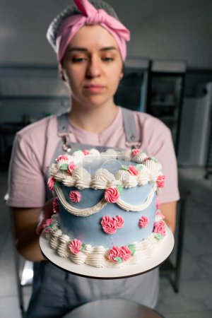 Téléchargez les photos : Gros plan dans une cuisine professionnelle une boulangère se tient debout avec un gâteau fini dans ses mains elle sourit - en image libre de droit