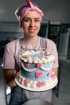 Photo for Close-up in a professional kitchen a female baker stands with a finished cake in her hands she smiling - Royalty Free Image