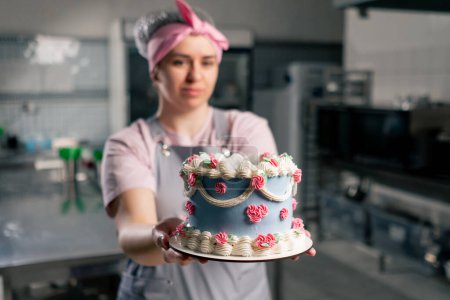 Foto de En una cocina profesional una pastelera está de pie con un pastel terminado en sus manos - Imagen libre de derechos