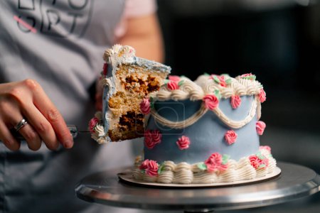 Téléchargez les photos : Gros plan dans une cuisine professionnelle un boulanger coupe un morceau de gâteau bleu avec un couteau - en image libre de droit
