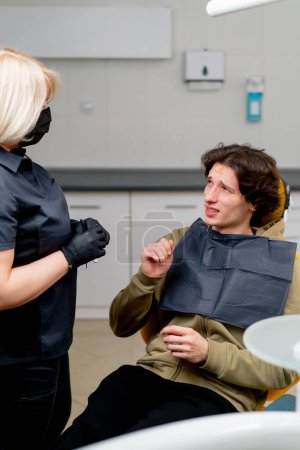 Téléchargez les photos : Cabinet dentaire dentiste blonde consulter un patient gars parlant de mauvaise dent - en image libre de droit