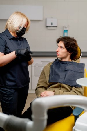 Foto de Odontólogo médico odontólogo rubio en uniforme negro consultar a un paciente - Imagen libre de derechos