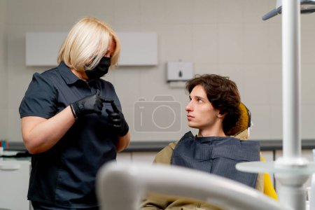 Photo for Dental office doctor blonde dentist in black uniform consulting a patient - Royalty Free Image