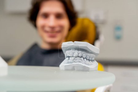 Téléchargez les photos : Gros plan dans un cabinet dentaire un jeune homme allongé sur la table avec un plâtre des dents des patients sur le fond - en image libre de droit
