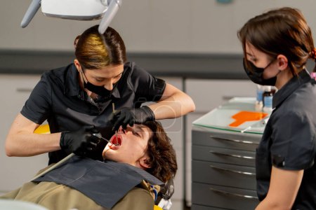 Téléchargez les photos : Dans le cabinet dentaire, une femme médecin examine la cavité buccale à l'aide d'un miroir et d'une machine à air - en image libre de droit