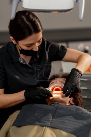 Téléchargez les photos : Dans le cabinet dentaire, une femme médecin examine la cavité buccale à l'aide d'un miroir et d'une machine à air - en image libre de droit