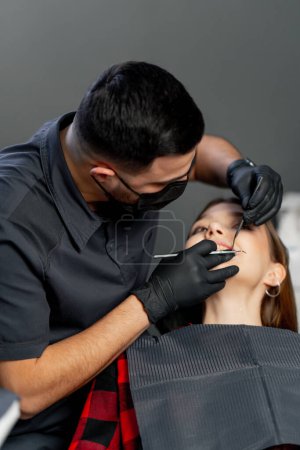 Foto de En un consultorio dental un dentista masculino examina los dientes de una joven hermosa - Imagen libre de derechos