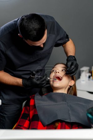 Photo for In a dental office a male dentist gives an anesthetic injection to a young beautiful girl - Royalty Free Image
