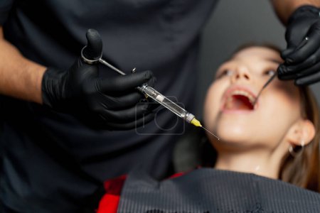 Téléchargez les photos : Dans un cabinet dentaire un dentiste donne une injection anesthésique à une jeune belle fille - en image libre de droit