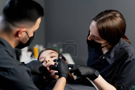 Foto de En un consultorio dental un dentista hombre con un asistente le da una inyección anestésica a una joven hermosa - Imagen libre de derechos