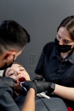 Photo for In a dental office a man dentist with an assistant gives an anesthetic injection to a young beautiful girl - Royalty Free Image