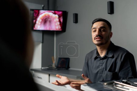 Foto de En un consultorio dental un hombre muestra una foto de los dientes en un monitor para una joven hermosa consulta de la muchacha - Imagen libre de derechos