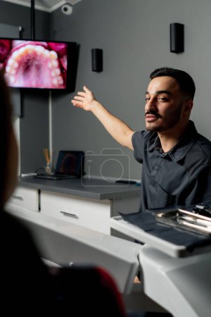 Photo for In a dental office a man shows a photo of teeth on a monitor for a young beautiful girl consultation - Royalty Free Image