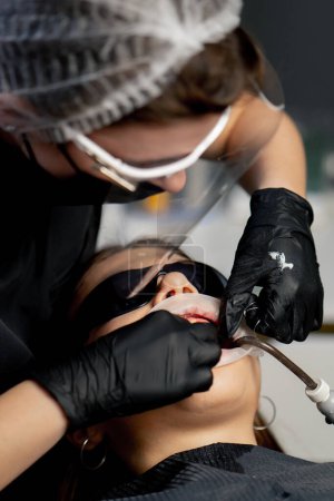 Téléchargez les photos : Dans un cabinet dentaire dentiste femme dans une casquette ne soie dentaire à une jeune belle fille - en image libre de droit