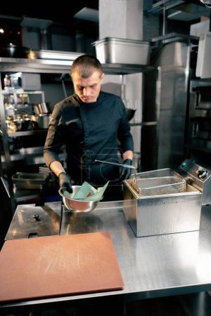 Foto de El chef en la cocina del establecimiento vierte batatas de la freidora en un tazón para enfriar - Imagen libre de derechos