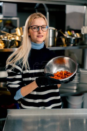 Photo for A young girl with glasses in the kitchen stands with a bowl of sweet potato demonstrating looking at the camera - Royalty Free Image