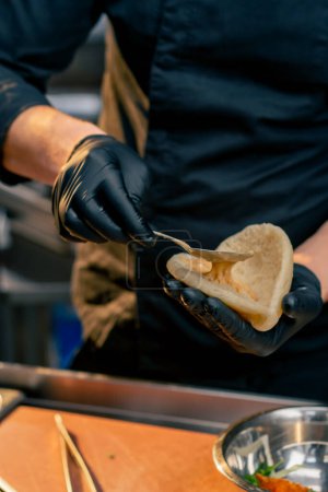 Foto de Primer plano de un chef en guantes negros poniendo diferentes salsas en un bollo con una cuchara - Imagen libre de derechos