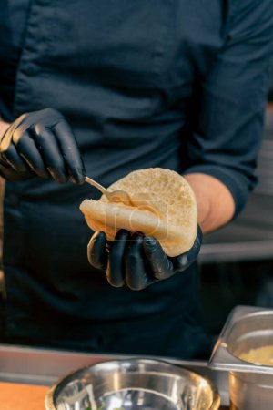 close-up of a chef in black gloves putting different sauces on a bun with a spoon