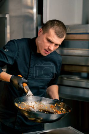 Téléchargez les photos : Gros plan d'un chef dans la cuisine tenant une poêle avec des nouilles se préparant à verser sur l'assiette - en image libre de droit