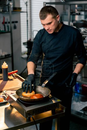 in the kitchen, a hand in a black glove places a bun on a hot frying pan
