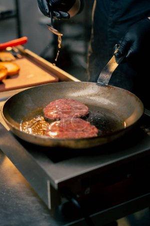 close-up in the kitchen of a restaurant pouring oil over beef cutlets in a frying pan