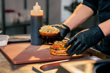 close-up of the chefs hands in the kitchen of the establishment covering the finished burger with one half of the bun