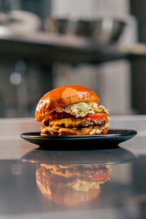 Foto de Primer plano de una hamburguesa grande ya hecha con carne de res en la cocina de un establecimiento acostado en un plato negro - Imagen libre de derechos