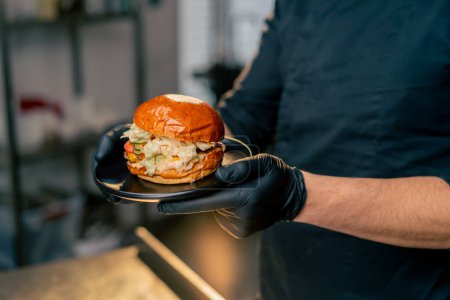 close-up of the hands of a chef in an establishment examining in his hands a ready-made burger lying on black plate