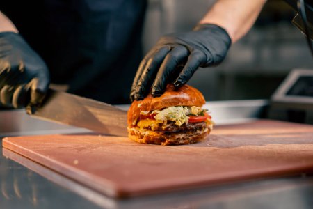 close-up of the hands of a chef in an establishment cutting a ready-made burger lying on a board with a knife