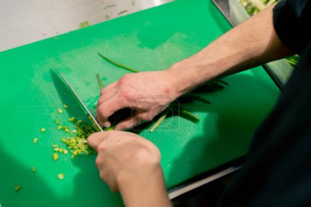 Photo for Close-up in the kitchen on a green board the process of cutting greens with a knife - Royalty Free Image