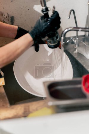 Téléchargez les photos : Gros plan d'une femme qui lave de la vaisselle sale dans la cuisine après avoir utilisé un équipement professionnel - en image libre de droit