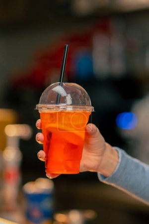 Photo for Close-up of a womans hand holding a ready-made orange cocktail with a straw - Royalty Free Image