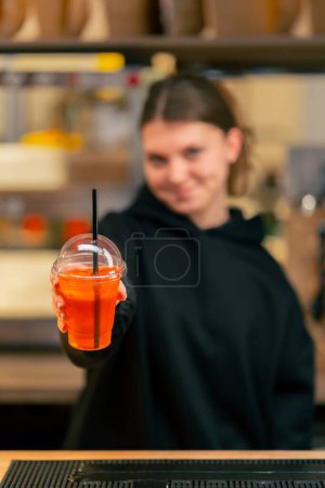 Foto de Una joven en un restaurante se para en el mostrador del bar con un cóctel en la mano y sonríe - Imagen libre de derechos